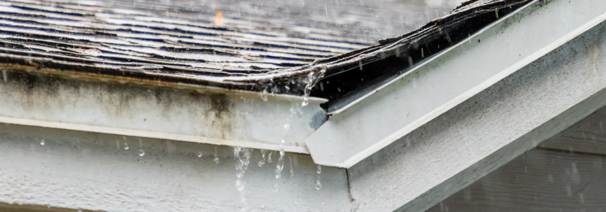 1 Close up shot of roof getting rained on with broken gutters and damaged shingles after a storm.