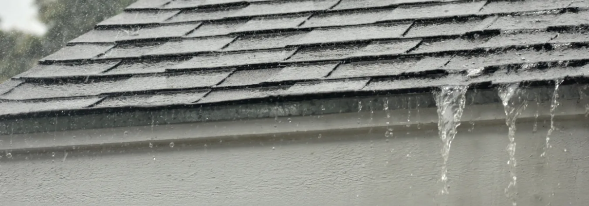 2 Rain from storm pouring from gutters on residential, asphalt shingles roof.