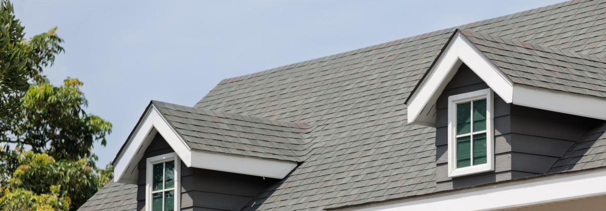 iStock 1398061041 Roof shingles with garret house on top of the house. dark asphalt tiles on the roof background on afternoon time. dark asphalt tiles on the roof background.