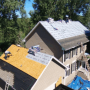 Roofing contractors working on residential roof surrounded by trees.