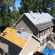 Roofing contractors working on residential roof surrounded by trees.